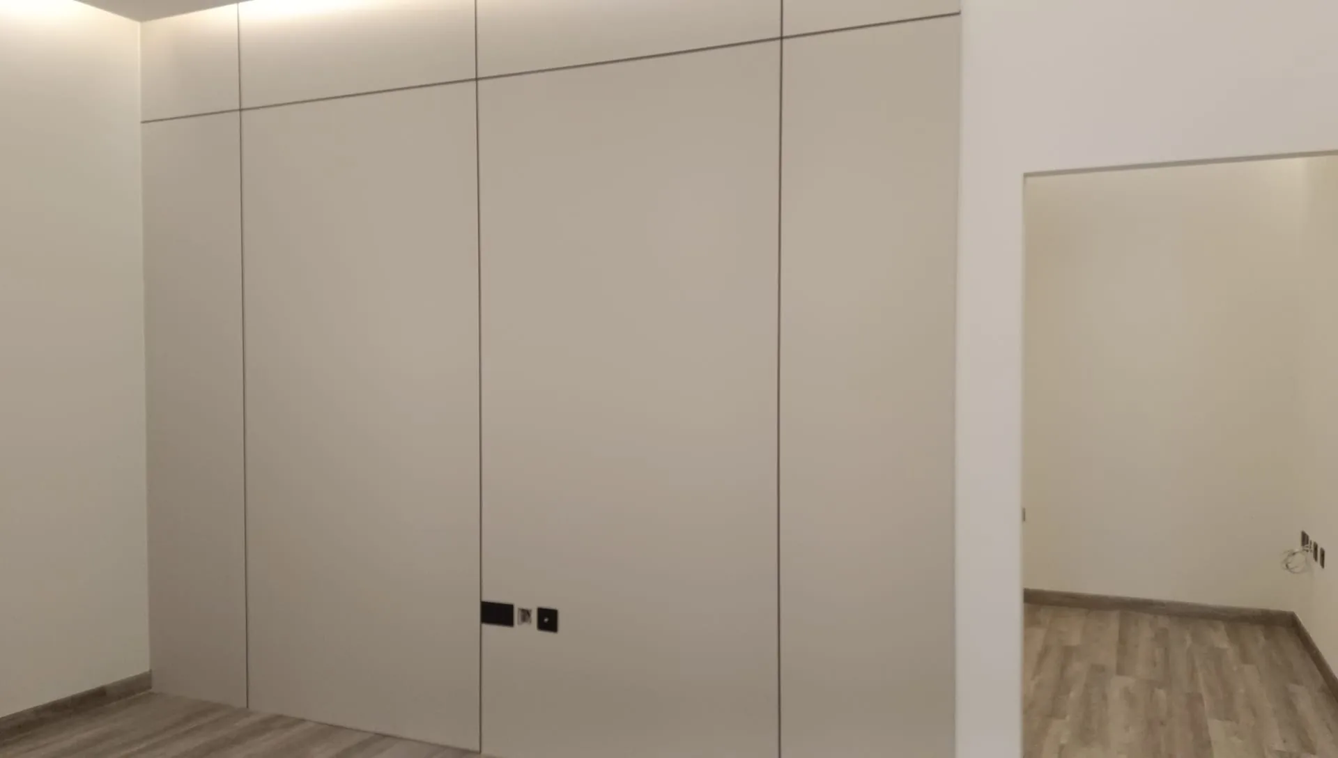 Handleless white fitted wardrobe spanning a bedroom wall floor to ceiling