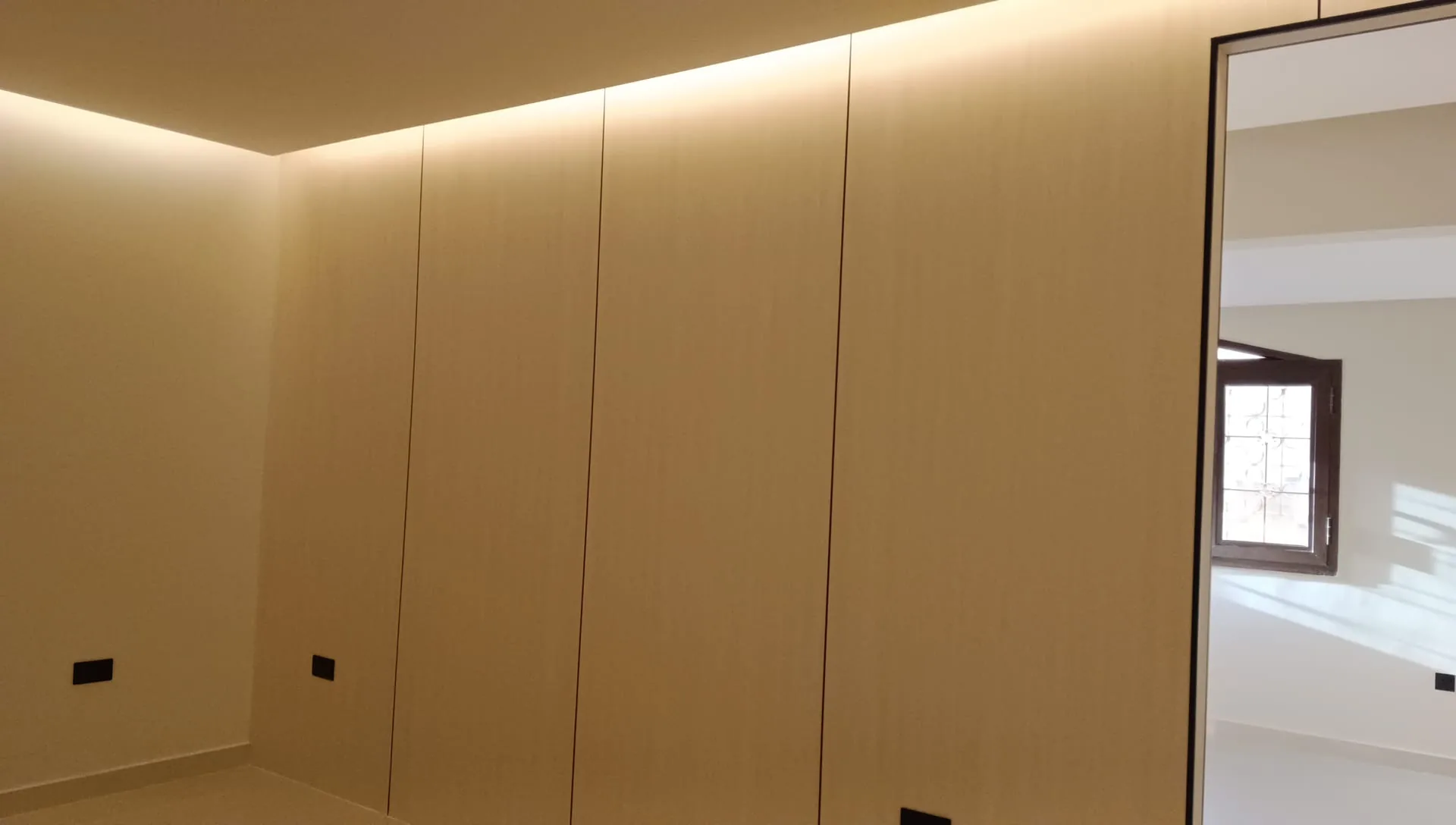 Handleless wood veneer wardrobe run finished flush to the ceiling with cove lighting