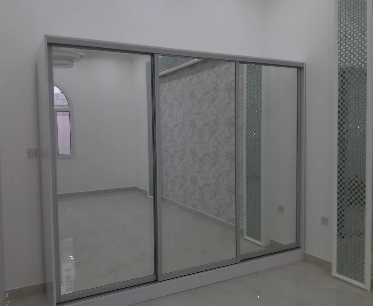 Three-door sliding mirrored wardrobe fitted in a Qatari bedroom